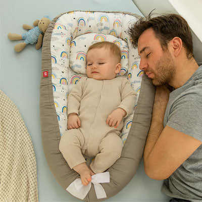 Père et bébé dormant paisiblement côte à côte dans un réducteur de lit bébé gris à motifs de sapins, garantissant un sommeil serein et protégé.