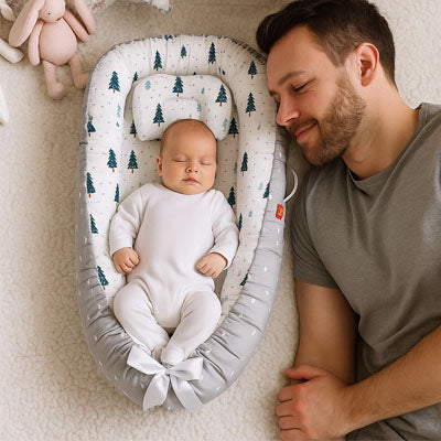 Père et bébé dormant paisiblement côte à côte dans un réducteur de lit bébé gris à motifs arc-en-ciel, pour un sommeil rassurant et doux.