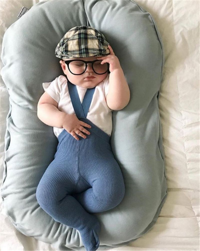 Un bébé portant des lunettes et une casquette dort dans un réducteur de lit biomimétique.