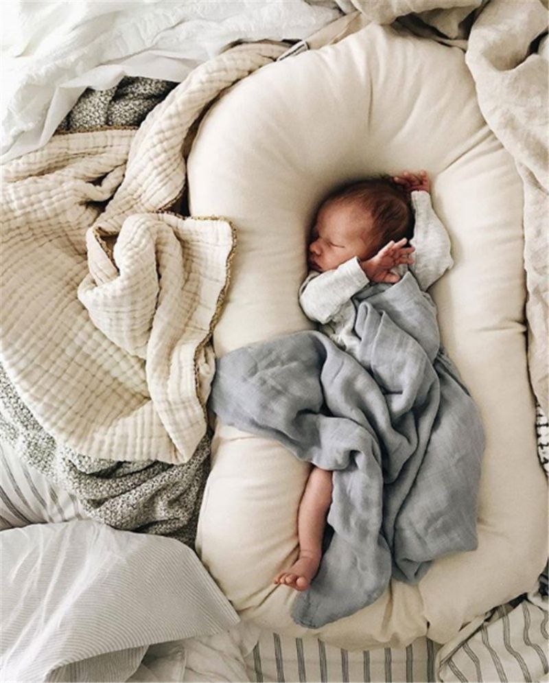 Un bébé est blotti dans un réducteur de lit biomimétique entouré de couvertures douces.